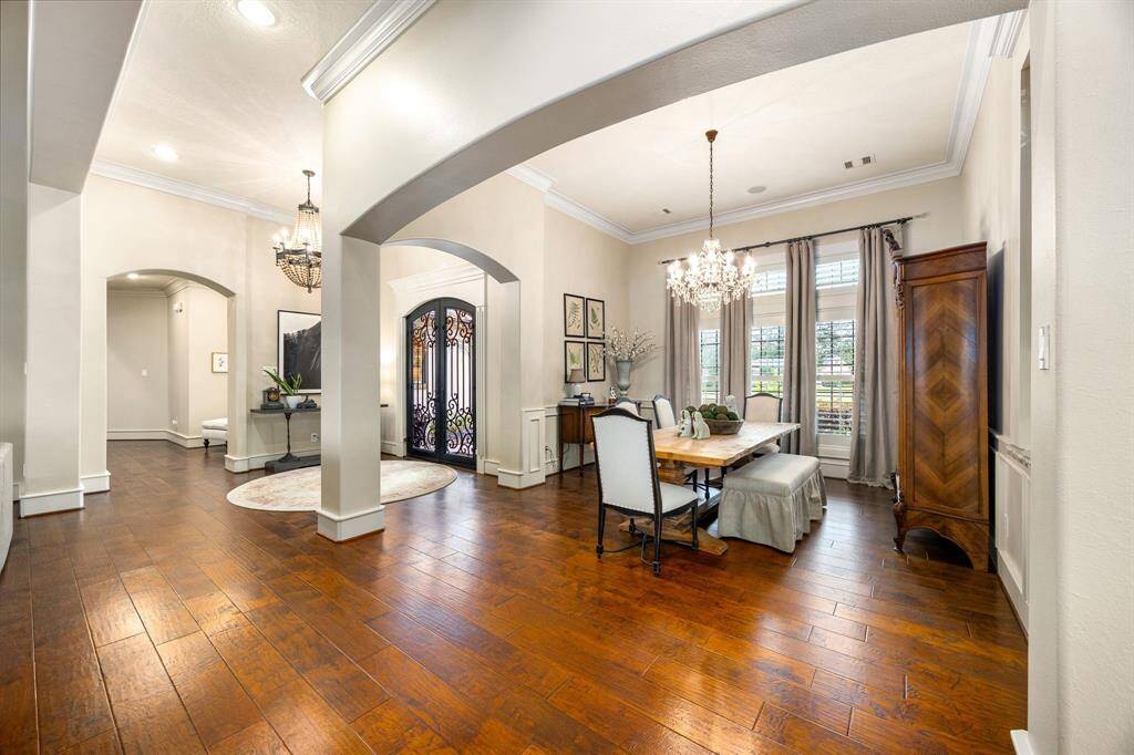 This elegant home features a spacious open entryway with rich hardwood flooring, high ceilings, and stylish chandeliers. The dining area is well-lit with large windows and classic decor, creating a warm and inviting atmosphere.