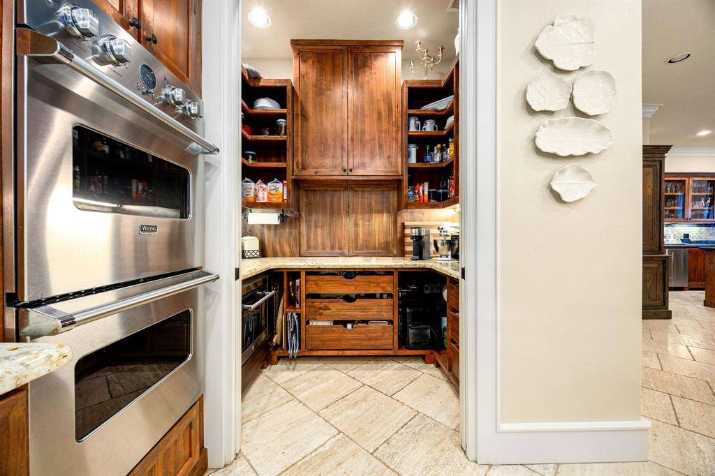 This walk-in pantry is a stunning extension of the kitchen, seamlessly combining beauty with exceptional functionality. Expertly designed with rich, built-in wood cabinetry and smart organizational features including a pass through door for ease in grocery drop off.