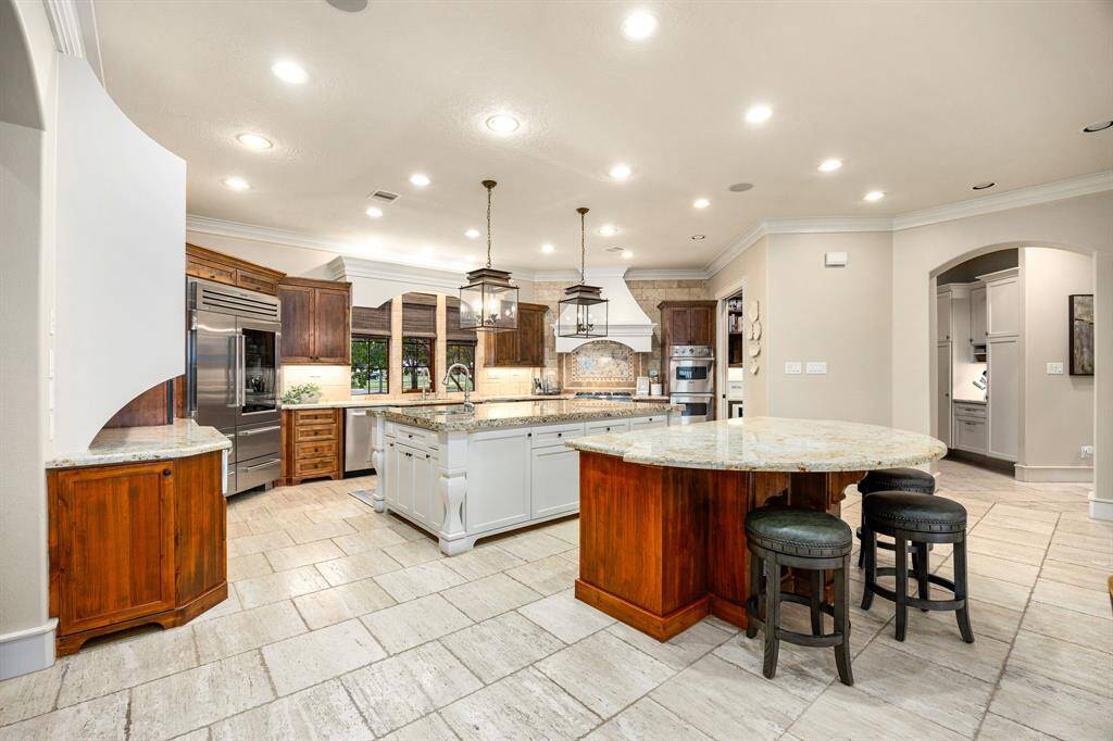 Two large pendant lights with bronze framing and glass panels illuminate the center island, adding a striking focal point that elevates the room's atmosphere. The second island enhances functionality, offering additional prep space, seating, or a dedicated area for entertaining.
