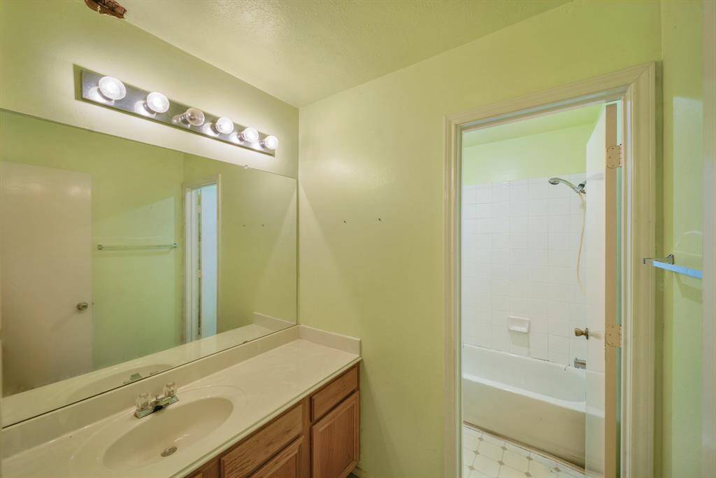This secondary bathroom features tile floors, a large mirror, wooden cabinetry, and a shower/tub combo.