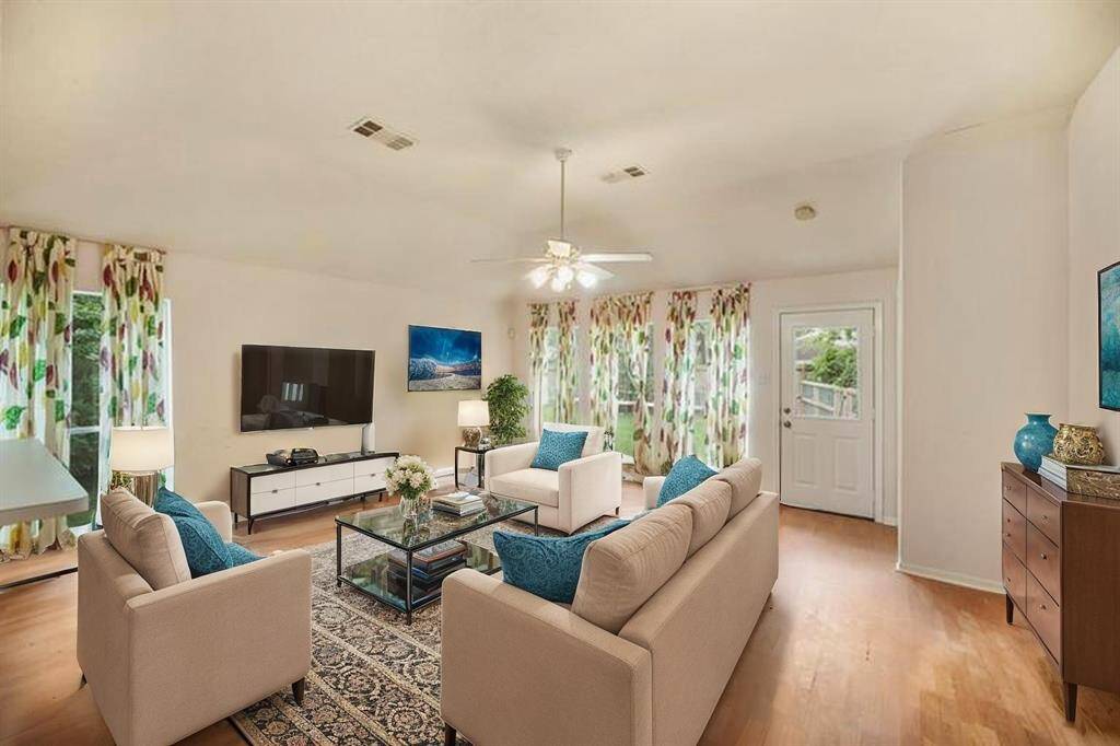 Virtually Staged: The spacious living room features wood floors, a ceiling fan, and large windows that will provide views into the backyard.
