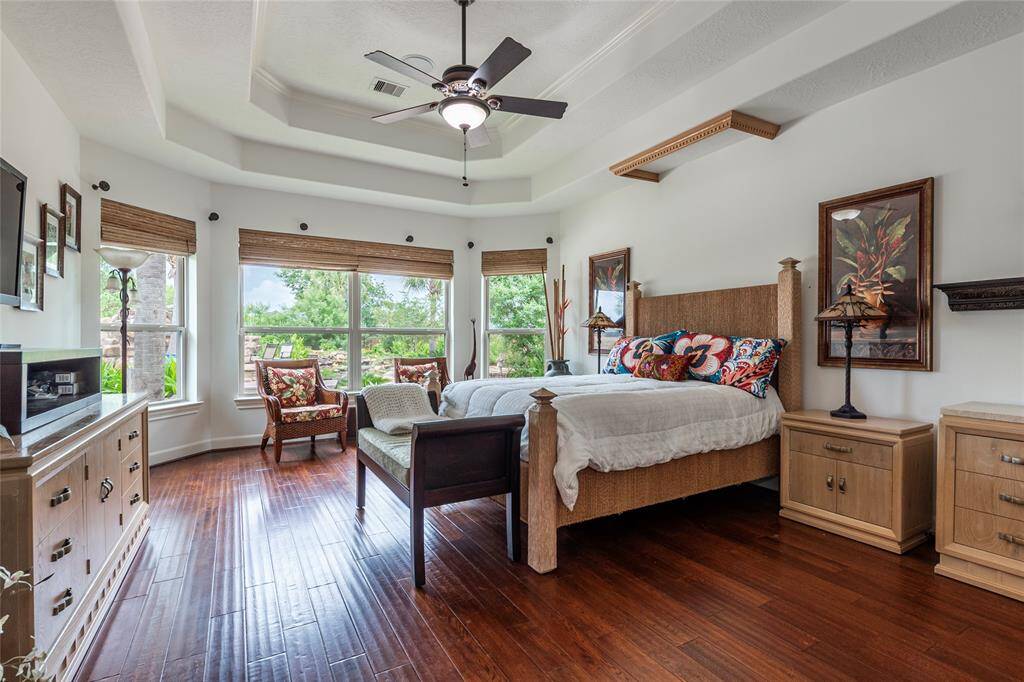 Located on the first floor, the spacious primary bedroom is a true retreat, featuring beautiful wood flooring and double trey ceilings that add a touch of grandeur. A cozy sitting area creates the perfect space to relax, while a wall of windows offers stunning views of the tropical backyard, bringing the outdoors in and filling the room with natural light.