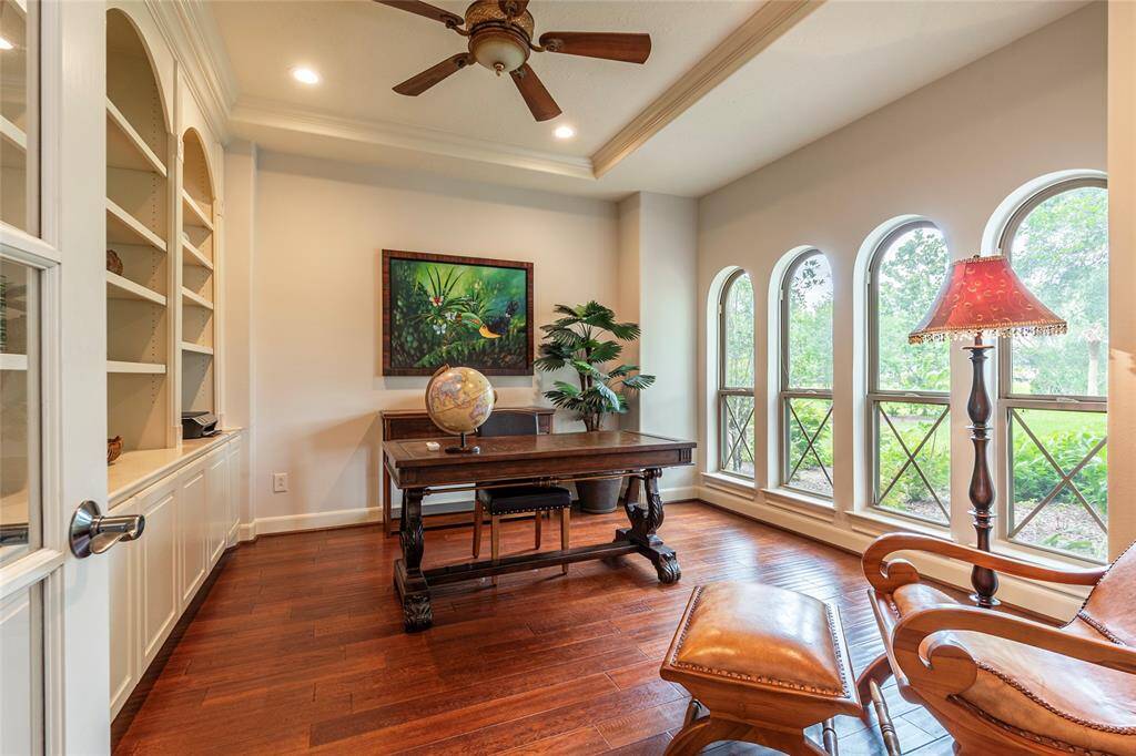 The spacious home office has been freshly painted and features French doors, rich wood flooring, a custom-built wall of bookshelves, and picturesque views of the manicured front landscaping—offering a serene and sophisticated setting for productivity.