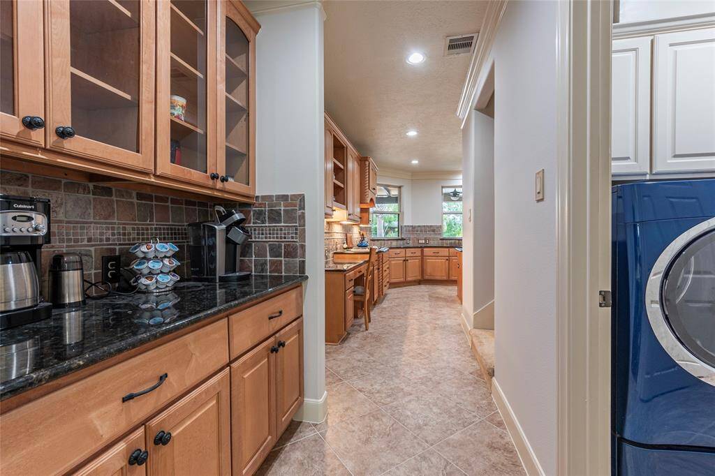Enjoy the convenience of a well-appointed butler’s pantry, featuring sleek granite countertops, elegant wood cabinetry, and glass cabinet doors that seamlessly extend into the kitchen area.