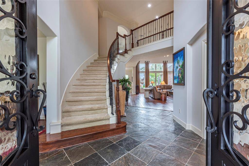 Recently installed custom cast iron double doors with glass accent ($9,800) make a bold statement as they open to a grand freshly painted entryway featuring elegant tile flooring, soaring ceilings, and a stunning winding wrought-iron staircase that sets the tone for the rest of this exquisite home.