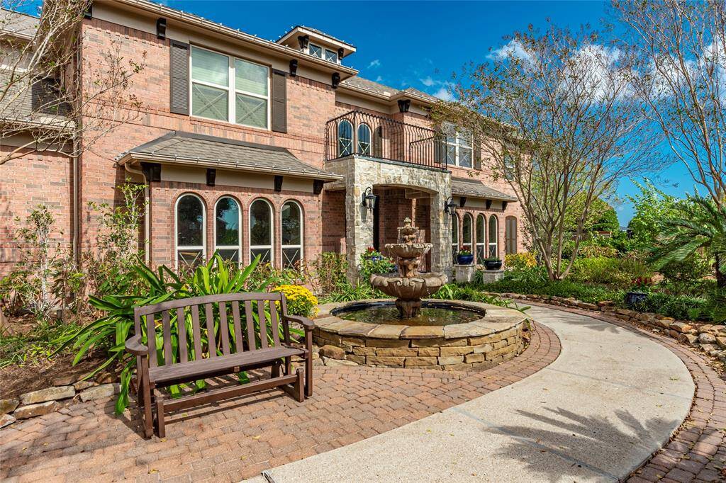 Prestigious Family Home In Gated Community.  Custom stone water fountain and lush landscaping lines the well designed brick-paver and concrete walkway leading front of the covered front porch.