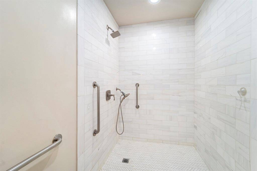 The en-suite bathroom features a walk-in marble-tiled shower that feels like a spa retreat. It's equipped with both a rainfall shower head and a handheld sprayer, giving you options for a relaxing or refreshing experience. The sleek tilework adds a touch of luxury, and the open design makes the space feel modern and bright.