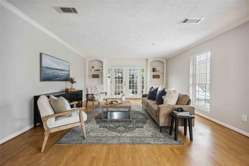 A light and bright living room accented with Crown molding, built-in shelving units, and French doors, offers a warm welcome.
