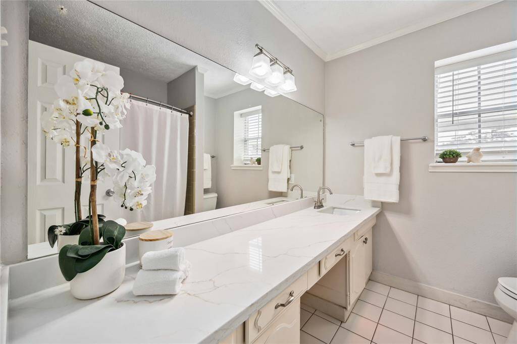 The primary bath features quartz counters atop a long vanity. Enjoy the elegant lighting.