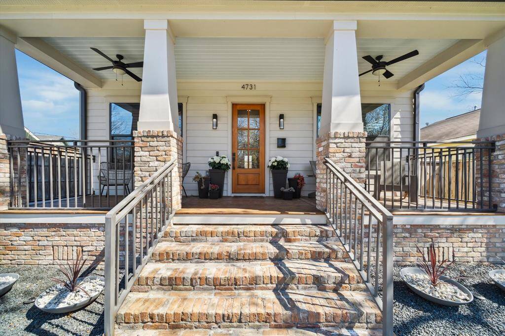 Charming front porch with brick accents and a wooden door. The space includes ceiling fans and a cozy seating area, perfect for relaxation.