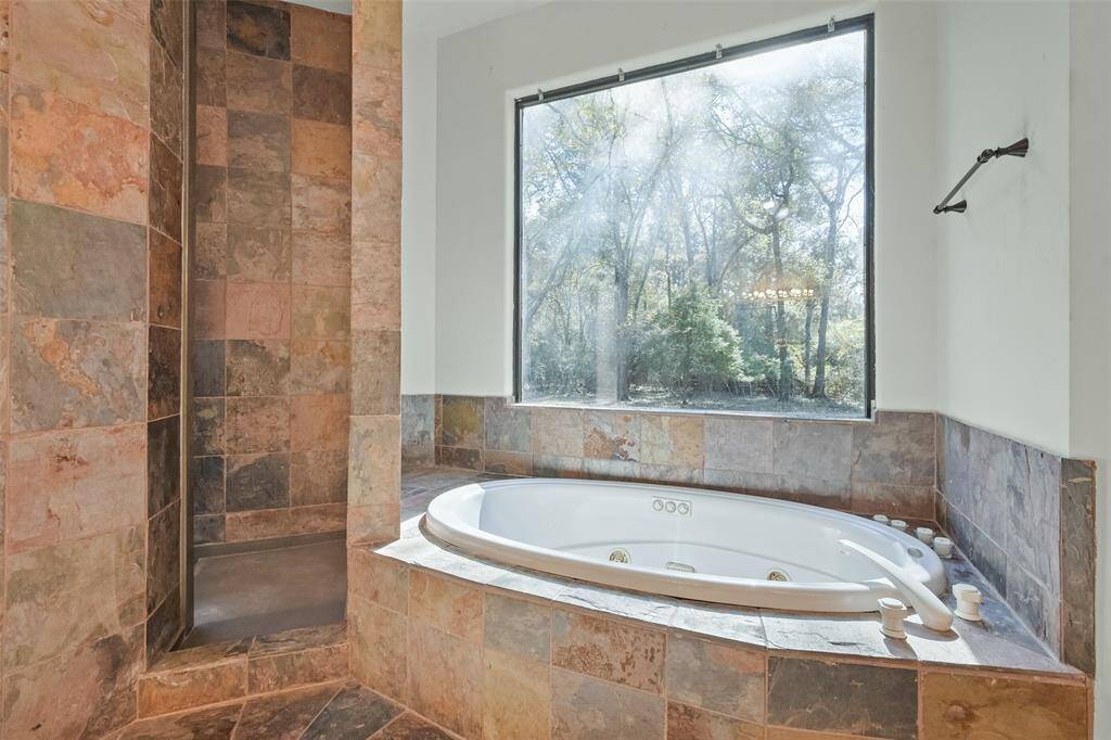 The jetted tub is set against a large window with a scenic view.