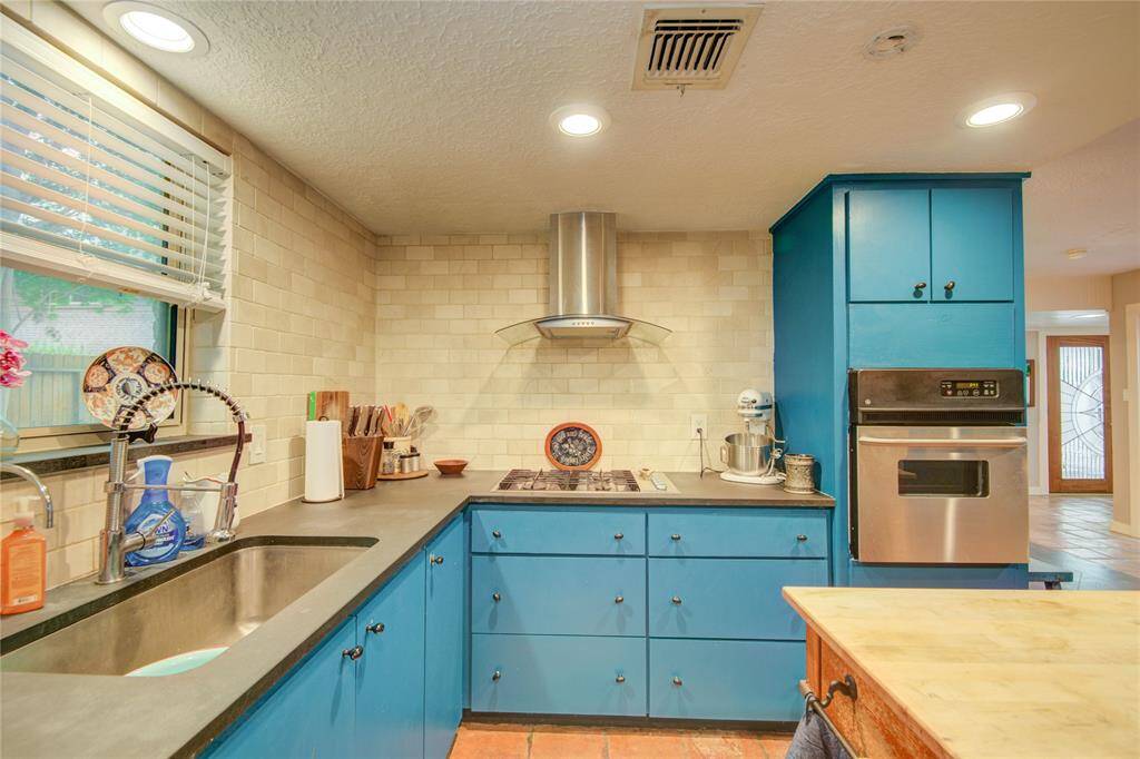 The kitchen features sleek stainless steel appliances and a modern steel-and-glass vent hood over the gas cooktop, combining style with functionality.