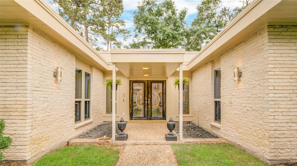 Elegant glass double doors welcome you through a charming courtyard-style entry framed by brick walls and greenery.