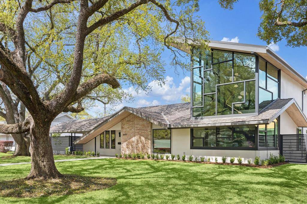 This modern home features a striking design with large glass DUAL pane LOW E-100 series windows by ANDERSEN, a sloped METAL roof, and a blend of brick and wood accents.