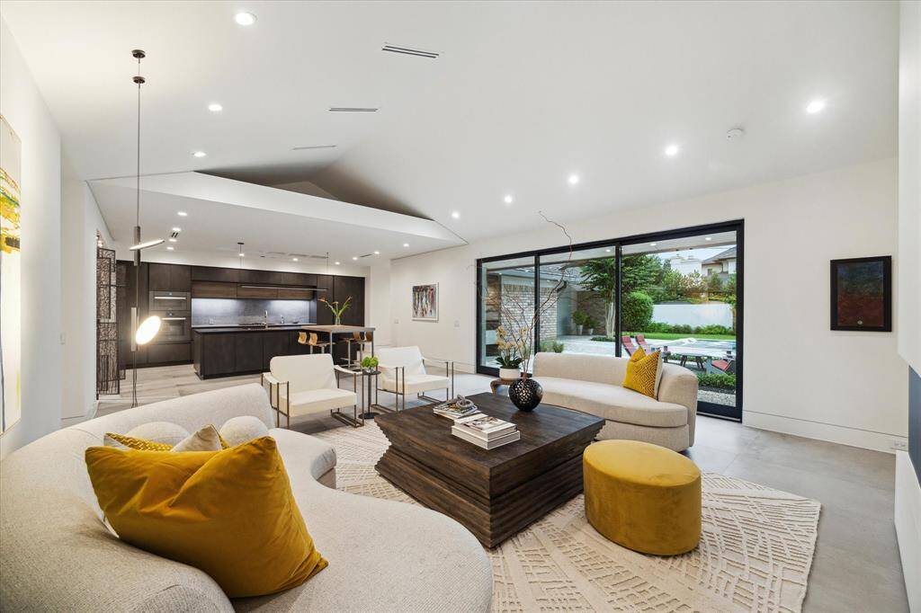 This modern living space features an open-concept design with a sleek kitchen, elegant seating area, and large sliding glass doors leading to a lush backyard. High ceilings and abundant natural light create an inviting atmosphere.