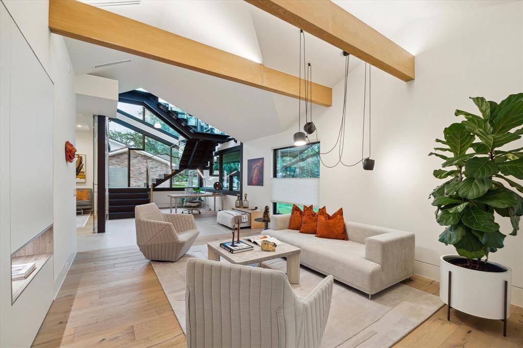 Upon entering, you'll be greeted by a grand room with high ceilings and exposed wooden beams. Large windows flood the space with natural light, and the sleek staircase provides a striking visual centerpiece.