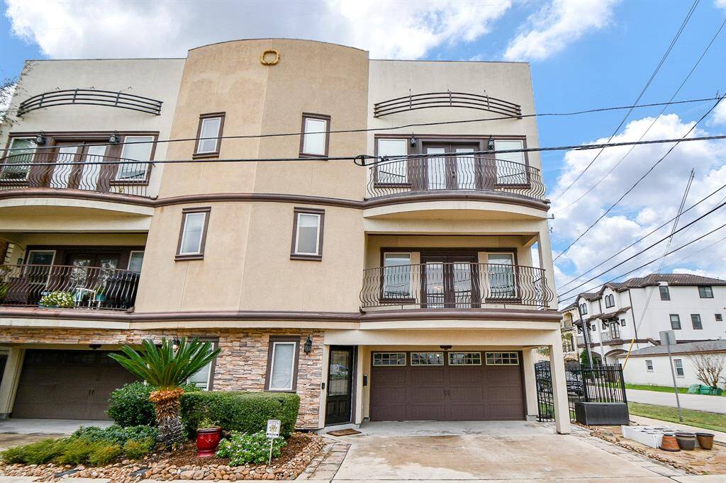 This is a modern, three-story townhouse featuring a stucco exterior with stone accents. It has multiple balconies, a two-car garage, and a small landscaped area at the front. Located in a neighborhood with similar style homes.