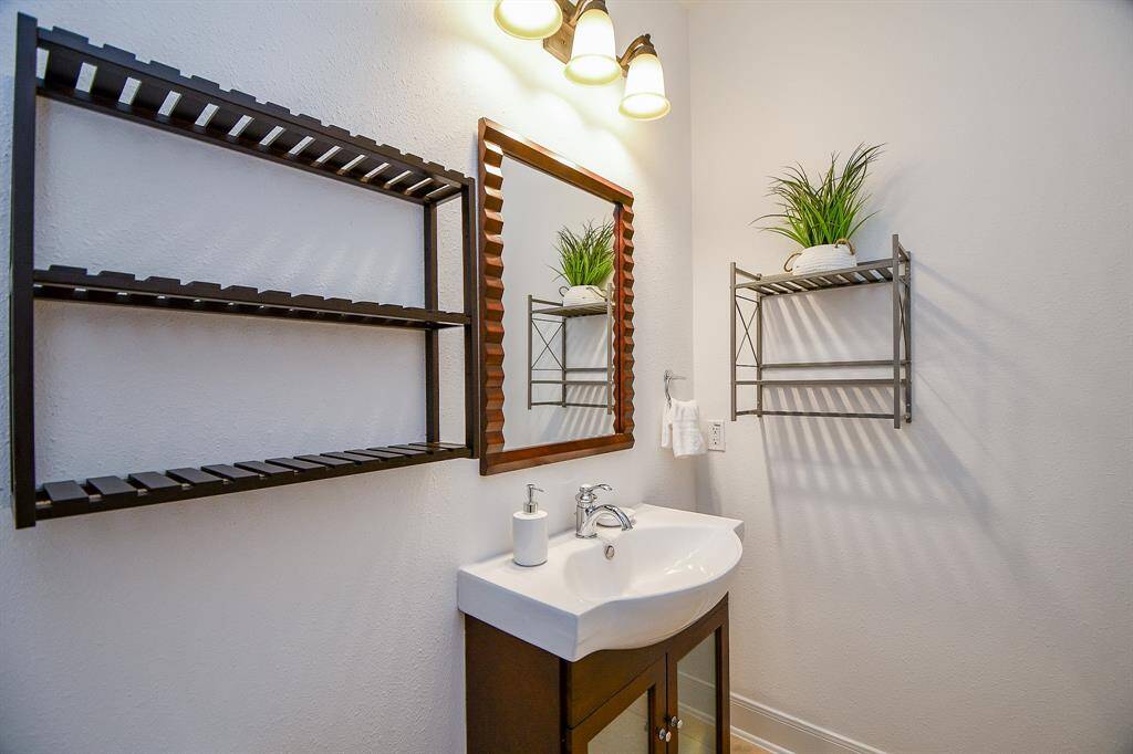 This bathroom features a modern design with a sleek white sink and vanity, stylish wall shelves for storage, and a decorative mirror. Soft lighting and a touch of greenery add warmth and elegance.