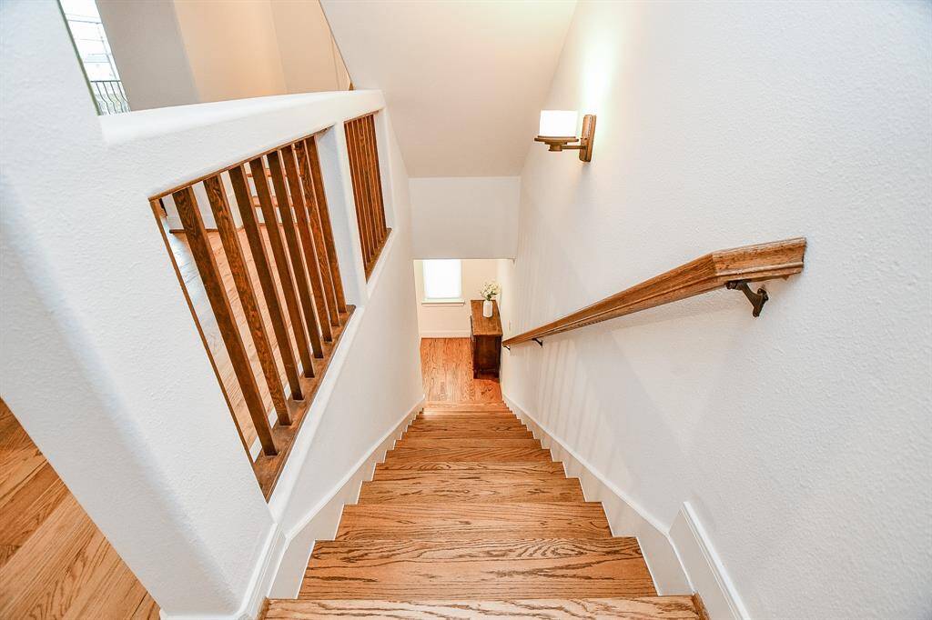 This photo showcases a well-lit, wooden staircase with a modern railing and wall-mounted light fixture, leading to a cozy landing area.