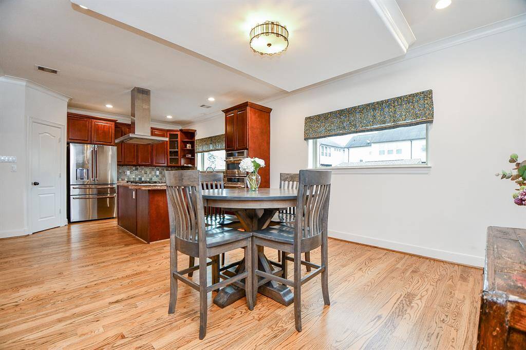 This photo showcases a spacious kitchen and dining area with hardwood floors, modern stainless steel appliances, and rich wooden cabinetry. A central dining table offers a cozy eating space, complemented by ample natural light from a large window.