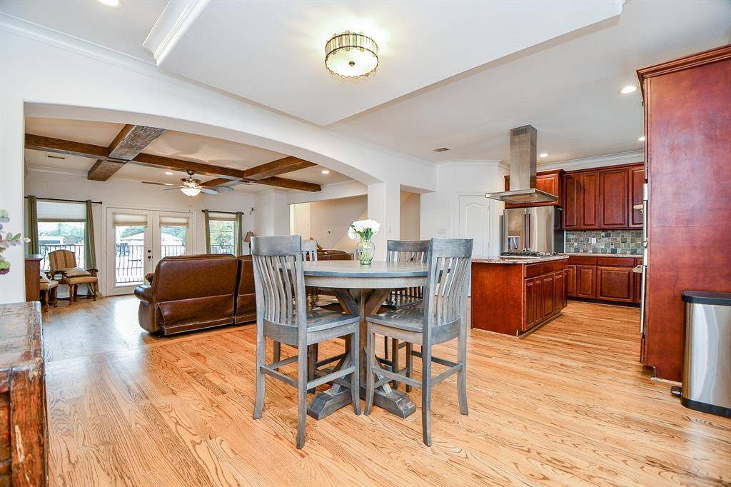 This open-concept area features a spacious kitchen with rich wood cabinetry and modern appliances, flowing into a cozy living room with wooden beam accents and French doors leading to an outdoor space. The hardwood floors and neutral tones enhance the inviting atmosphere.