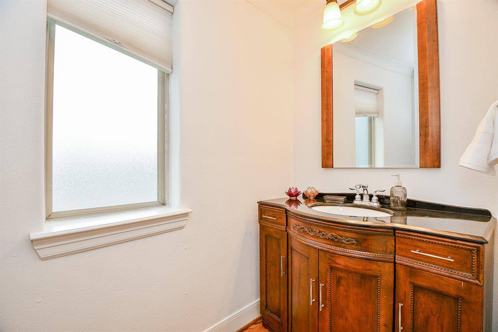 This photo shows a bright bathroom with a frosted window, a wooden vanity with a granite countertop, and a large mirror. The space is well-lit with overhead lighting.