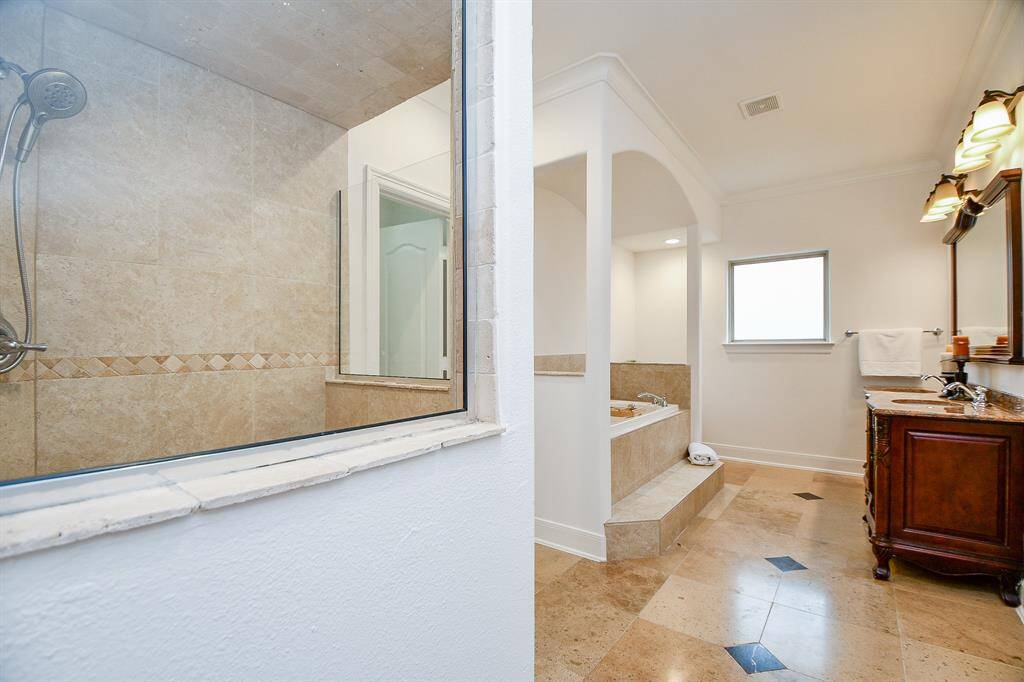 This bathroom features a spacious layout with a tiled walk-in shower, a separate bathtub, and a dual-sink vanity with elegant lighting and cabinetry. The room is well-lit with natural light from a frosted window.