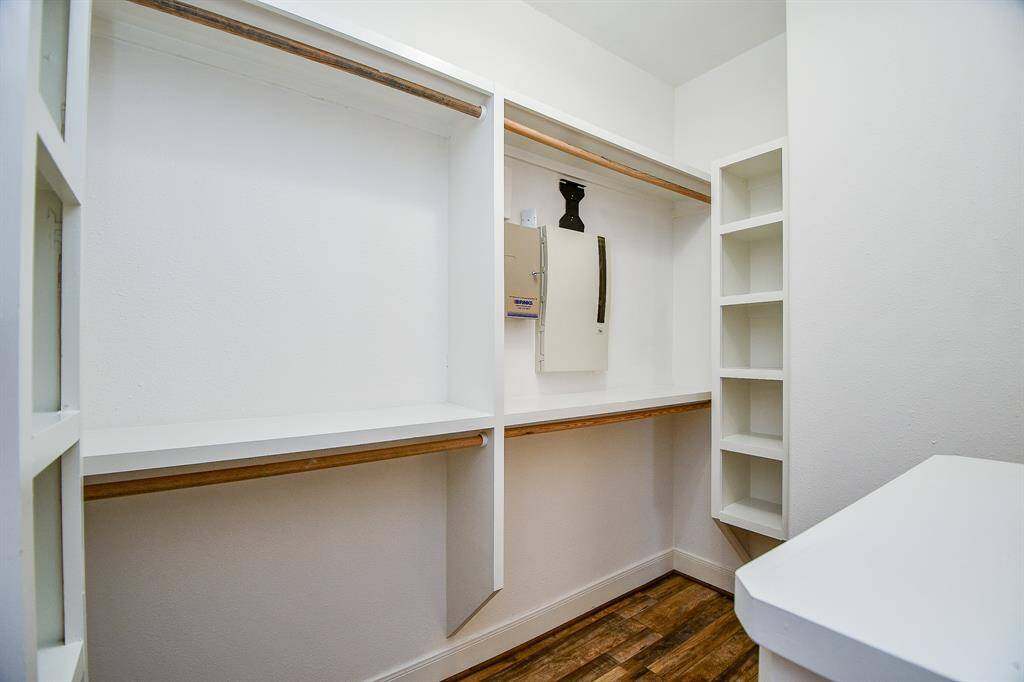 This is a spacious walk-in closet with built-in shelving and hanging rods. The closet features a wooden floor and white walls, providing ample storage and a clean look.