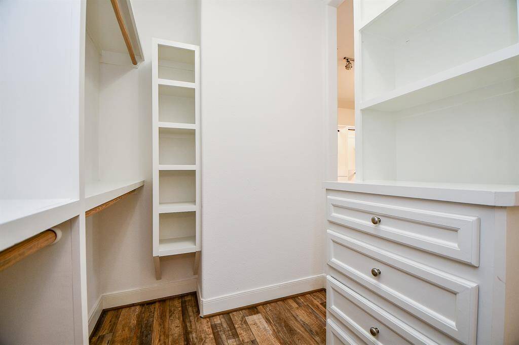 This photo showcases a spacious walk-in closet with built-in shelving and drawers, featuring a hardwood floor and ample storage options.