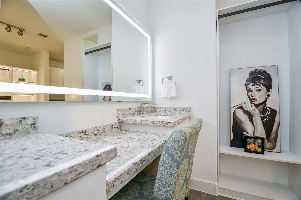 This photo showcases a modern bathroom vanity area with a large illuminated mirror and elegant granite countertops. The space includes a stylish chair and decorative artwork, creating a chic and functional setting.