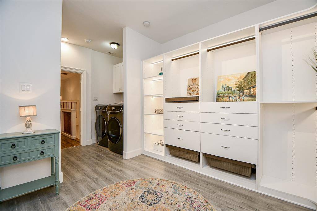 This photo showcases a bright and functional laundry room with modern appliances, ample built-in storage, and a stylish wood-look floor. A cozy side table with a lamp adds a decorative touch.