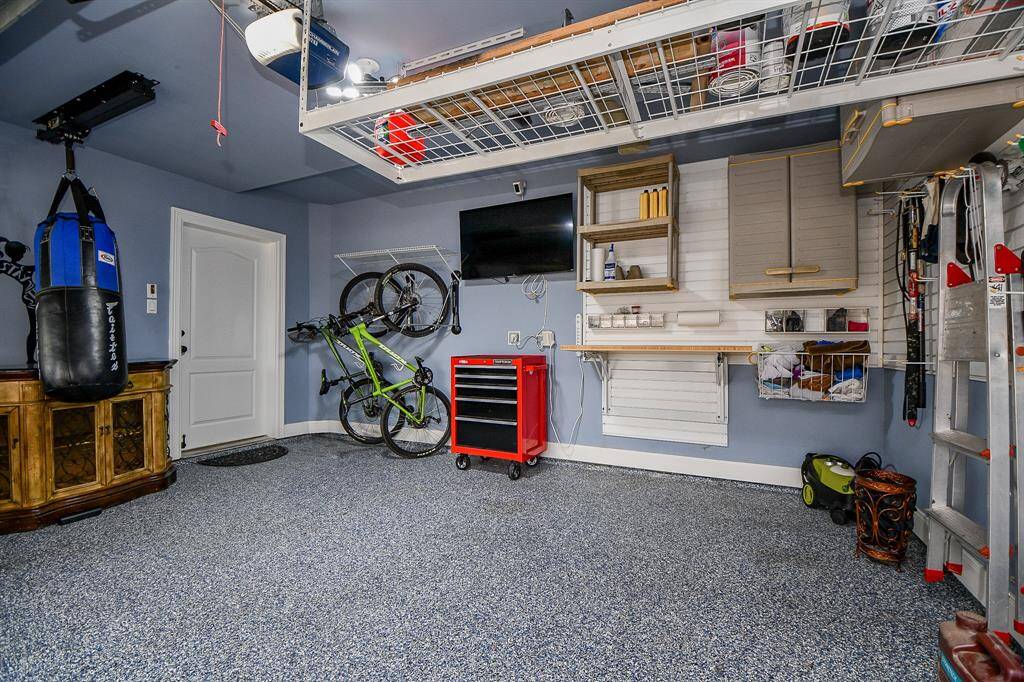 The photo shows a well-organized garage with a speckled floor, wall-mounted storage, and a hanging bike. There’s a punching bag, a red tool cart, and a ceiling rack for extra storage, creating a functional and tidy space.