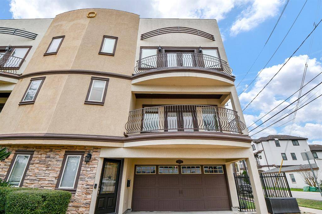Modern three-story townhouse with a stucco and stone exterior. It features two balconies with wrought iron railings and a two-car garage. The facade combines contemporary design with classic elements, offering curb appeal in a residential neighborhood.