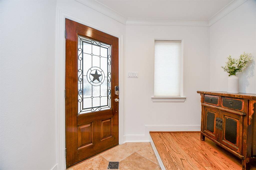 This welcoming entryway features a beautiful wooden front door with decorative glass, a small window for natural light, and a charming wooden console. The space combines tile and hardwood flooring, creating a warm and inviting atmosphere.