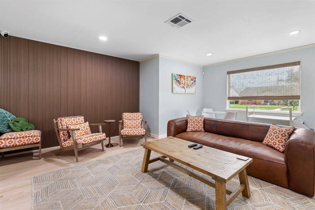 The spacious living room is the perfect space to relax and features refinished wood floors, recessed lights, accent wall and window covering