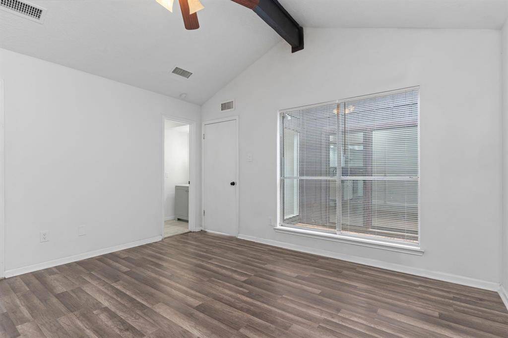 Private tucked away primary bedroom suite with high vaulted ceilings, ceiling fan, and no carpet but the carefree vinyl like wood flooring. Retreat to your peaceful primary suite with wood-look flooring, ceiling fan, and dramatic vaulted ceilings with exposed beam accents.