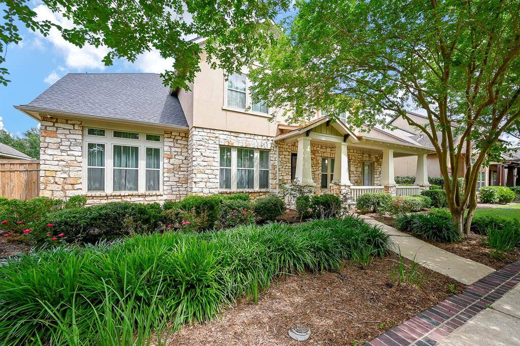 Charming home with a stone facade, inviting front porch, and lush landscaping. Features a well-maintained pathway and mature trees, offering great curb appeal.