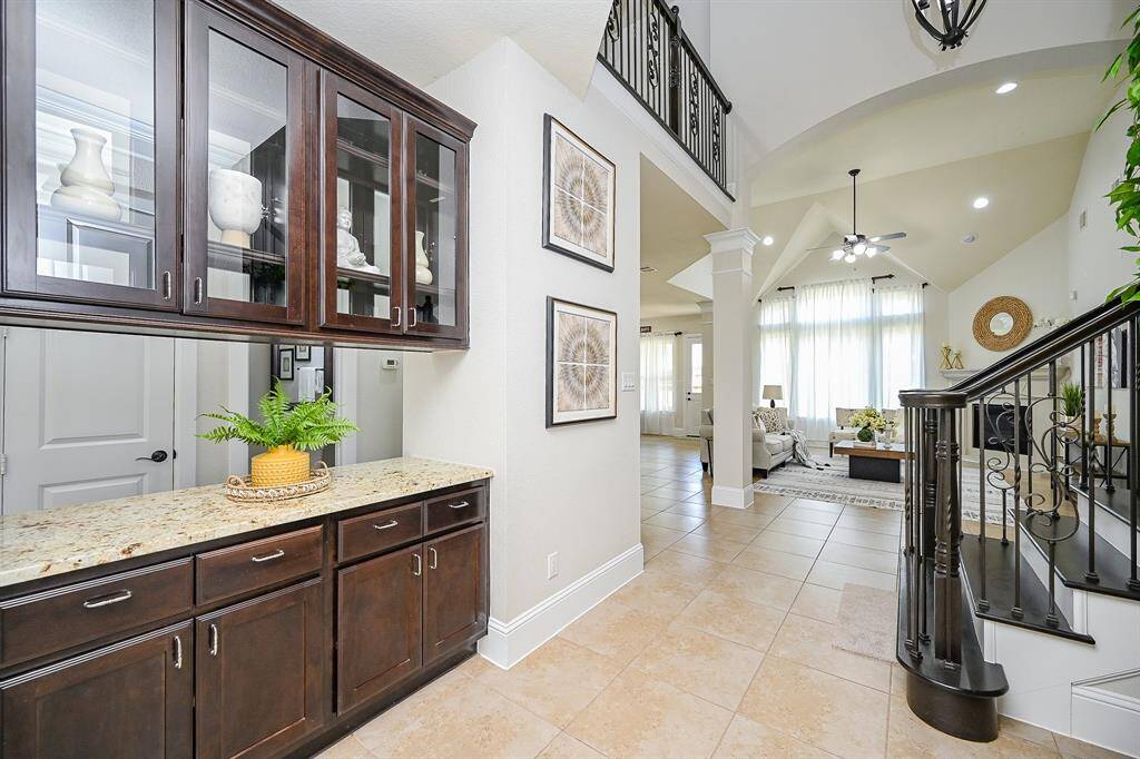 This inviting home features an elegant entryway with tiled floors, a staircase with wrought iron railings, and a cozy living area. The space is bright and open, with large windows allowing natural light to flood in. The built-in cabinetry and granite countertops add a touch of luxury and functionality.