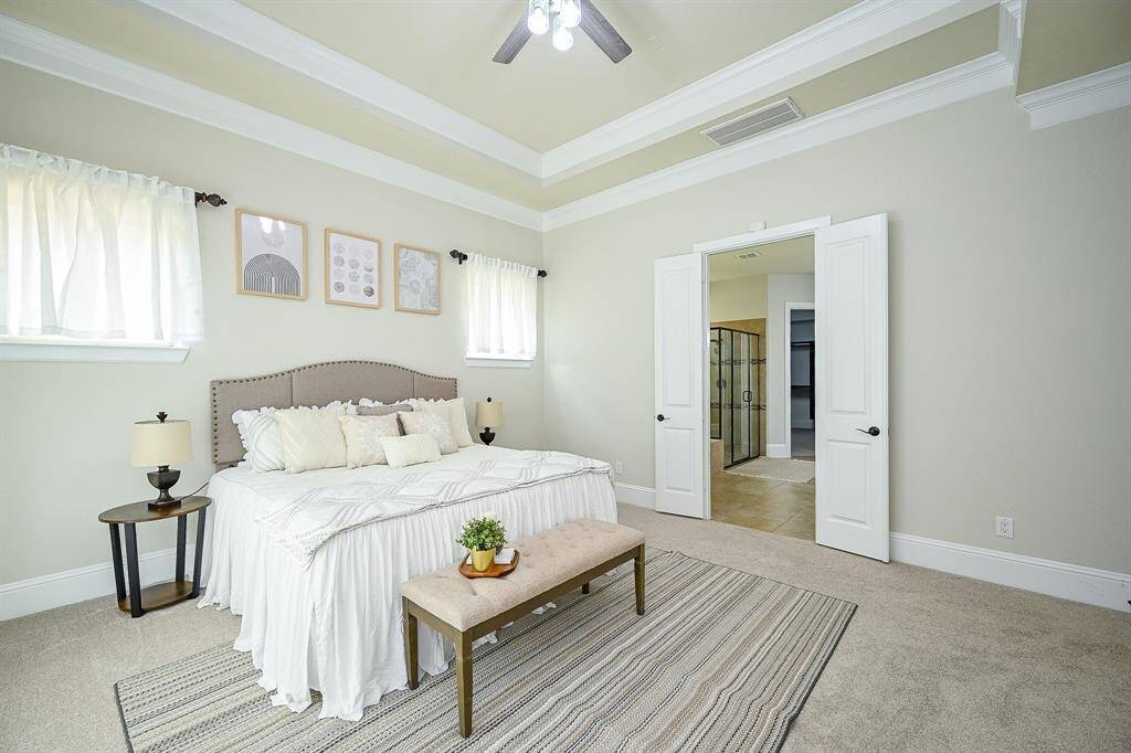 The primary bedroom features double doors leading to an en-suite bathroom with a glass shower. The room has ample natural light and tasteful decor.