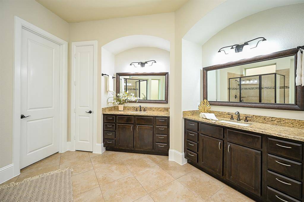 The spacious bathroom offers ample storage, large mirrors, and elegant lighting. The neutral tile flooring complements the clean and sophisticated design.