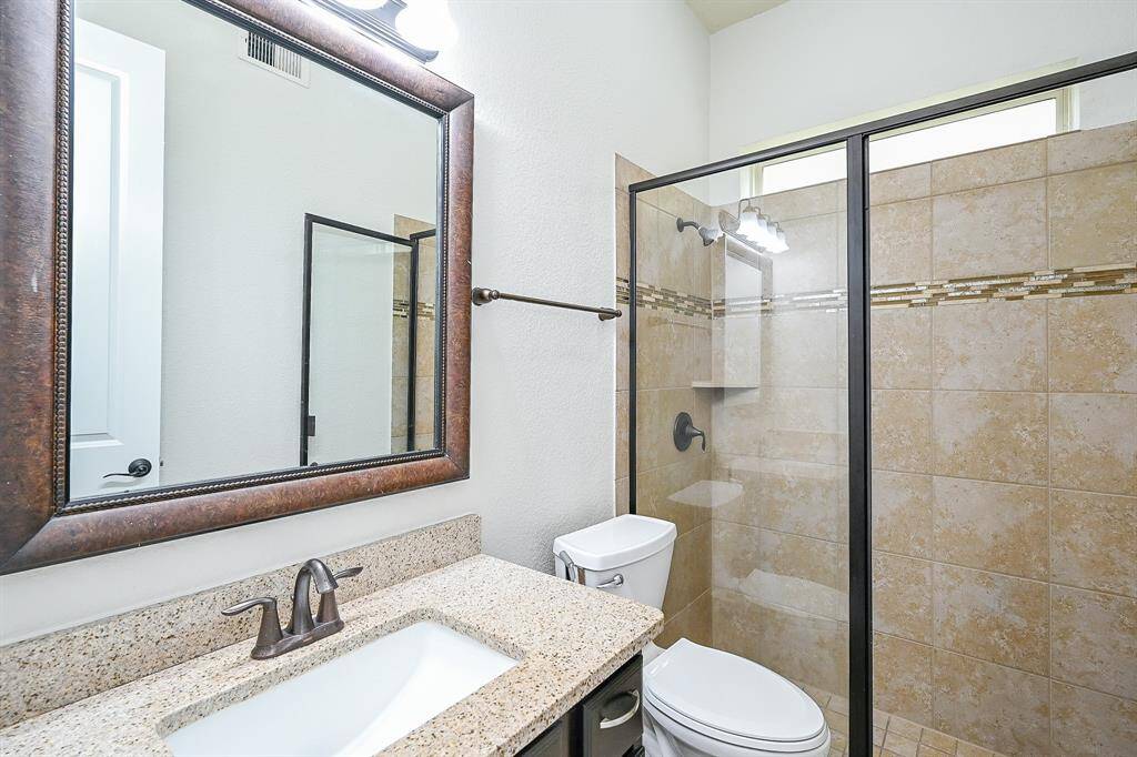 This full second bathroom down features a modern design with a large framed mirror, a granite countertop, and a sleek undermount sink. It includes a tiled walk-in shower with a glass door and a stylish accent strip, complemented by a contemporary faucet and fixtures.