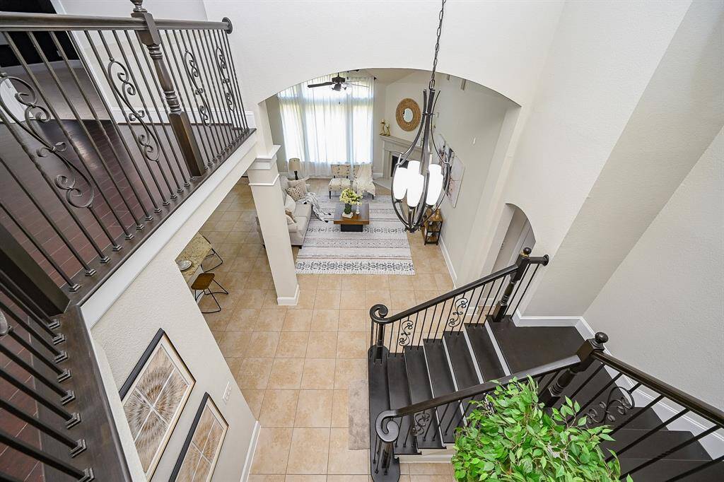 A bright and spacious two-story living area. The view from the staircase reveals elegant iron railings, and a cozy sitting area.
