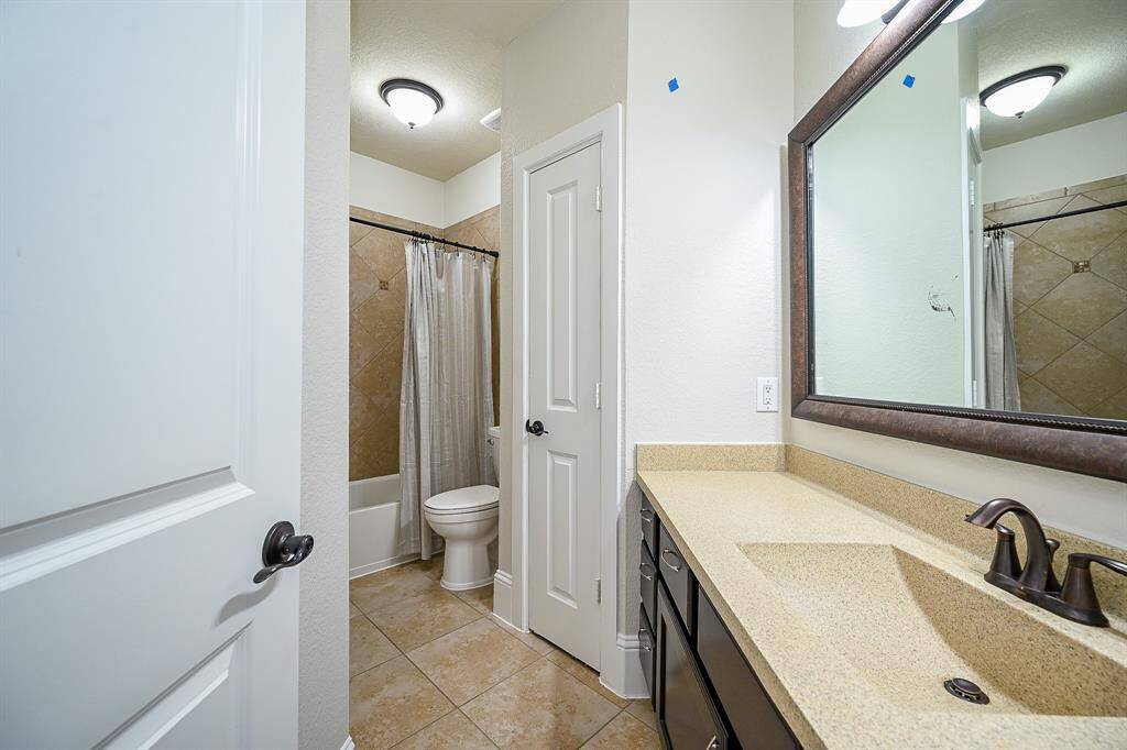 The secondary bathroom features a spacious vanity with a large mirror and ample storage. It includes a shower-tub combo and well-lit with ceiling lights.