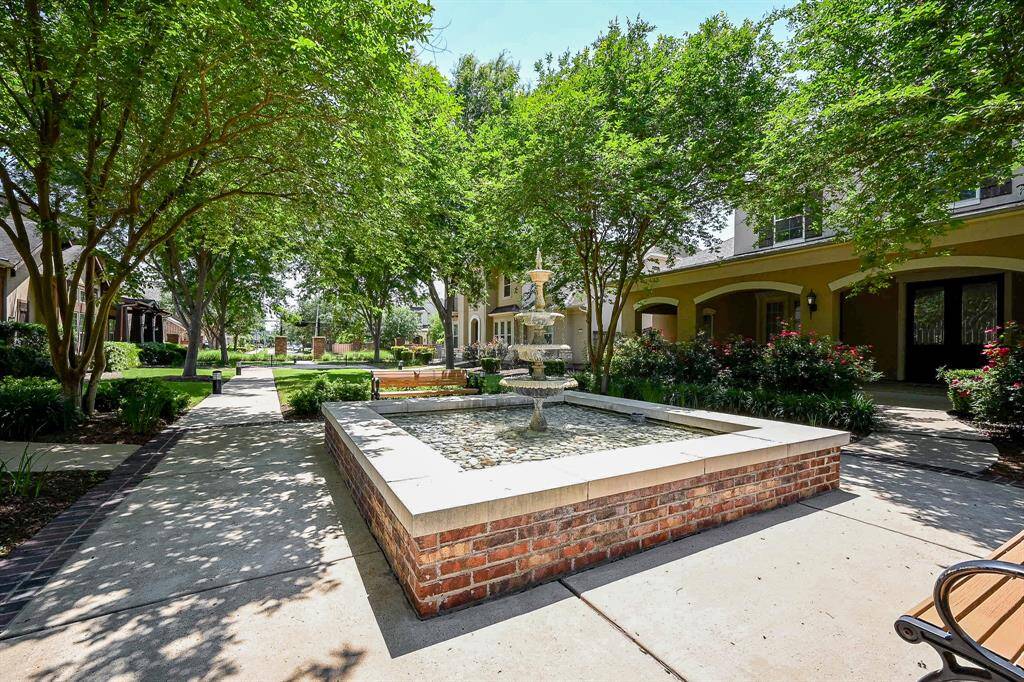 A serene courtyard with a charming stone fountain, surrounded by lush greenery and shaded pathways. It's an inviting and peaceful outdoor space, perfect for relaxation and leisure.