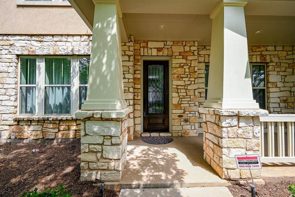 The covered area features sturdy columns, a decorative door, and a small garden space for added curb appeal.