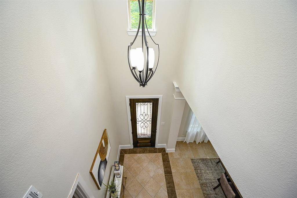 The two-story entryway with a decorative chandelier, tiled flooring, and an elegant wooden front door featuring glass and iron detailing.