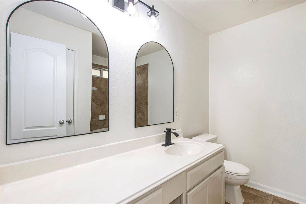 The primary bathroom boasts a freshly painted vanity that matches the kitchen’s style, with plenty of space for storage and everyday essentials. Two brand-new mirrors and sleek light fixtures enhance the modern, cohesive look, creating a functional and stylish area.