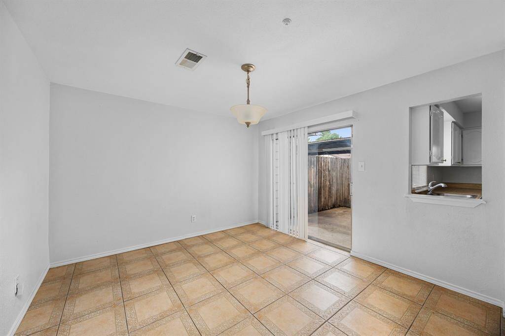 This room features a neutral color scheme with tile flooring, a ceiling light fixture, and sliding glass doors leading to an outdoor area. A pass-through window connects to the kitchen, enhancing the open feel.