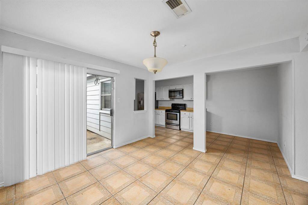 Bright dining area with tile flooring, sliding glass doors leading to a patio, and adjacent kitchen featuring stainless steel appliances and white cabinetry. Neutral tones create a versatile space.