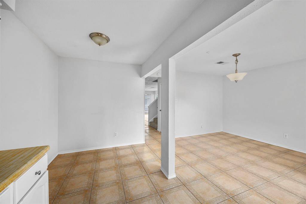 This photo shows a spacious, open-concept area with tiled flooring and neutral walls. It features two ceiling lights and a view of a staircase, creating a versatile space that can serve as both dining and living areas.